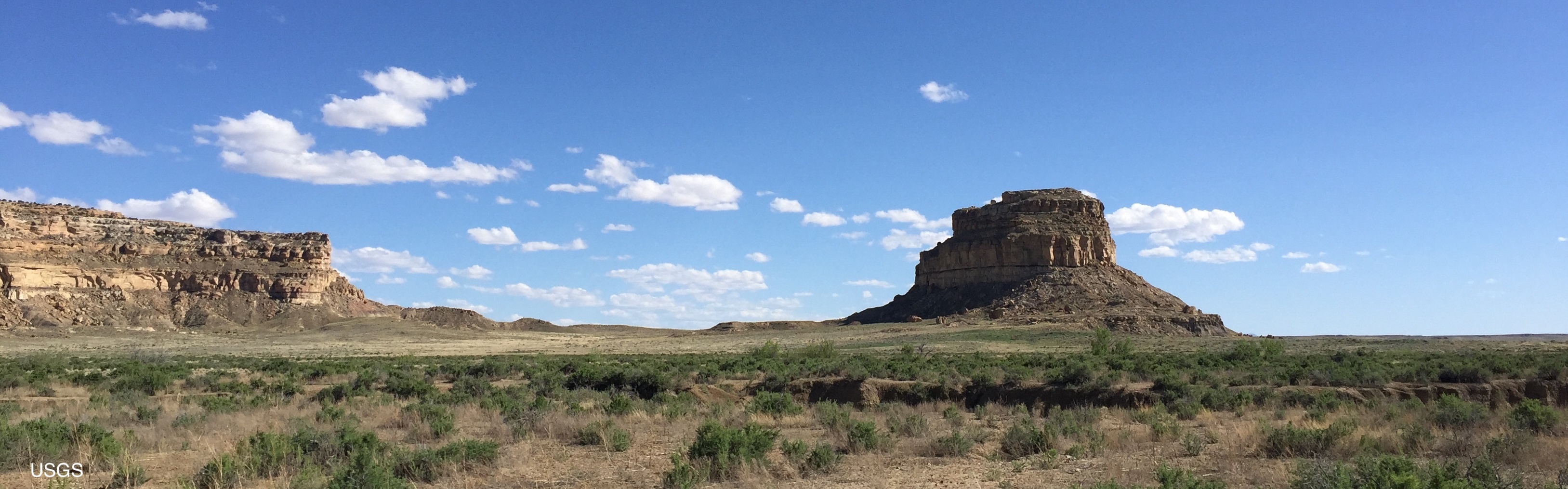 One platue and a butte landform across from one another in a dessert during the day
