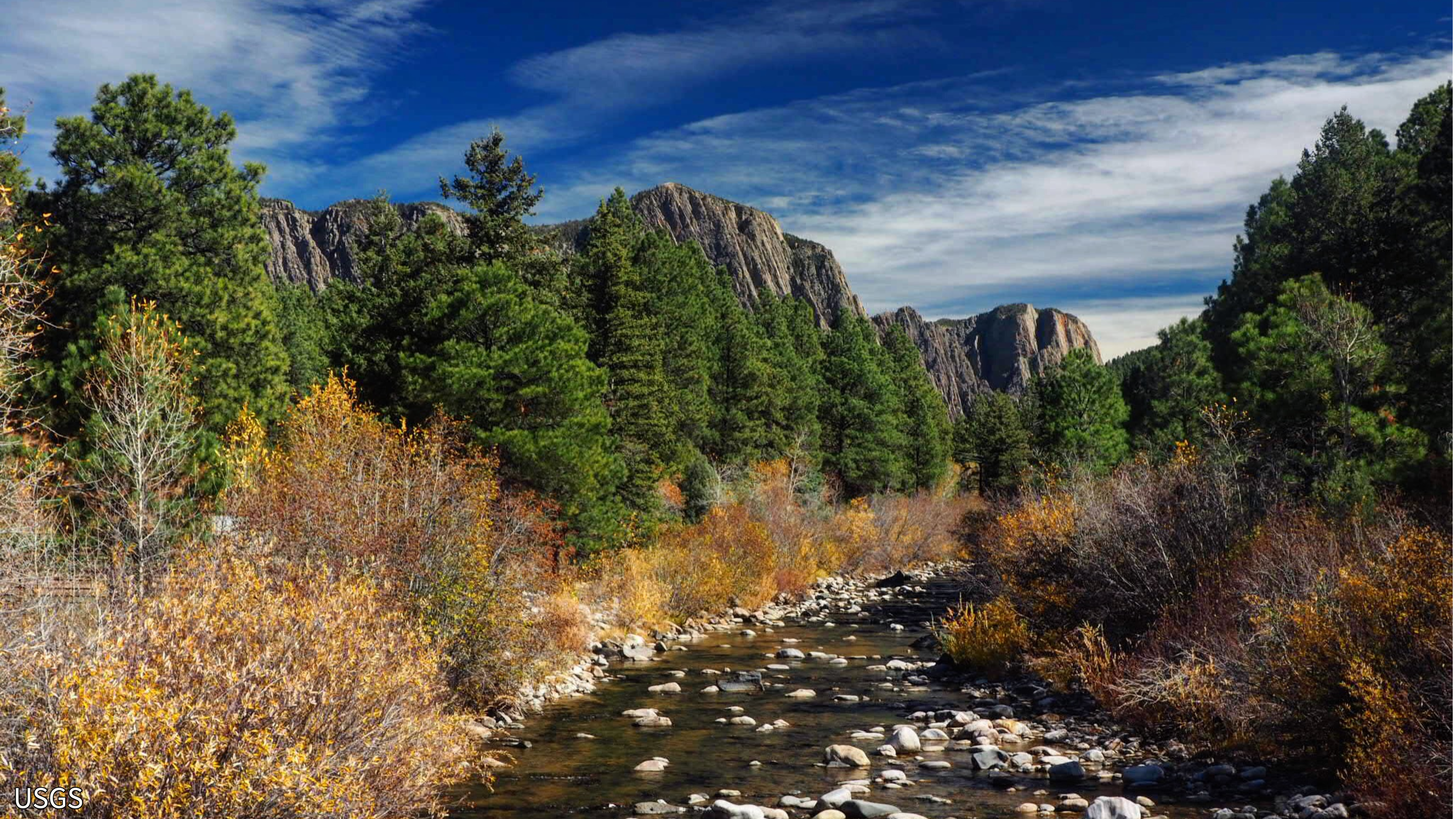 A river runs between two maintains with green and yellowing trees.